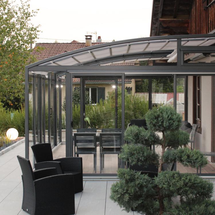 Abri de terrasse Vöroka modèle Topaz avec vitrage verre sécurité
										contre une maison comtoise